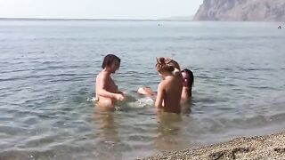 Three girls without tops pose on the beach with a beautiful view