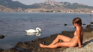 A girl is completely naked on the river bank and enjoys herself