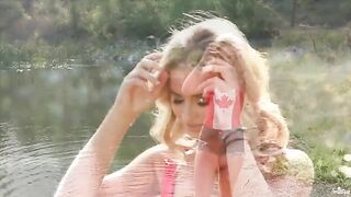 A blonde girl caresses herself tenderly on the lake shore